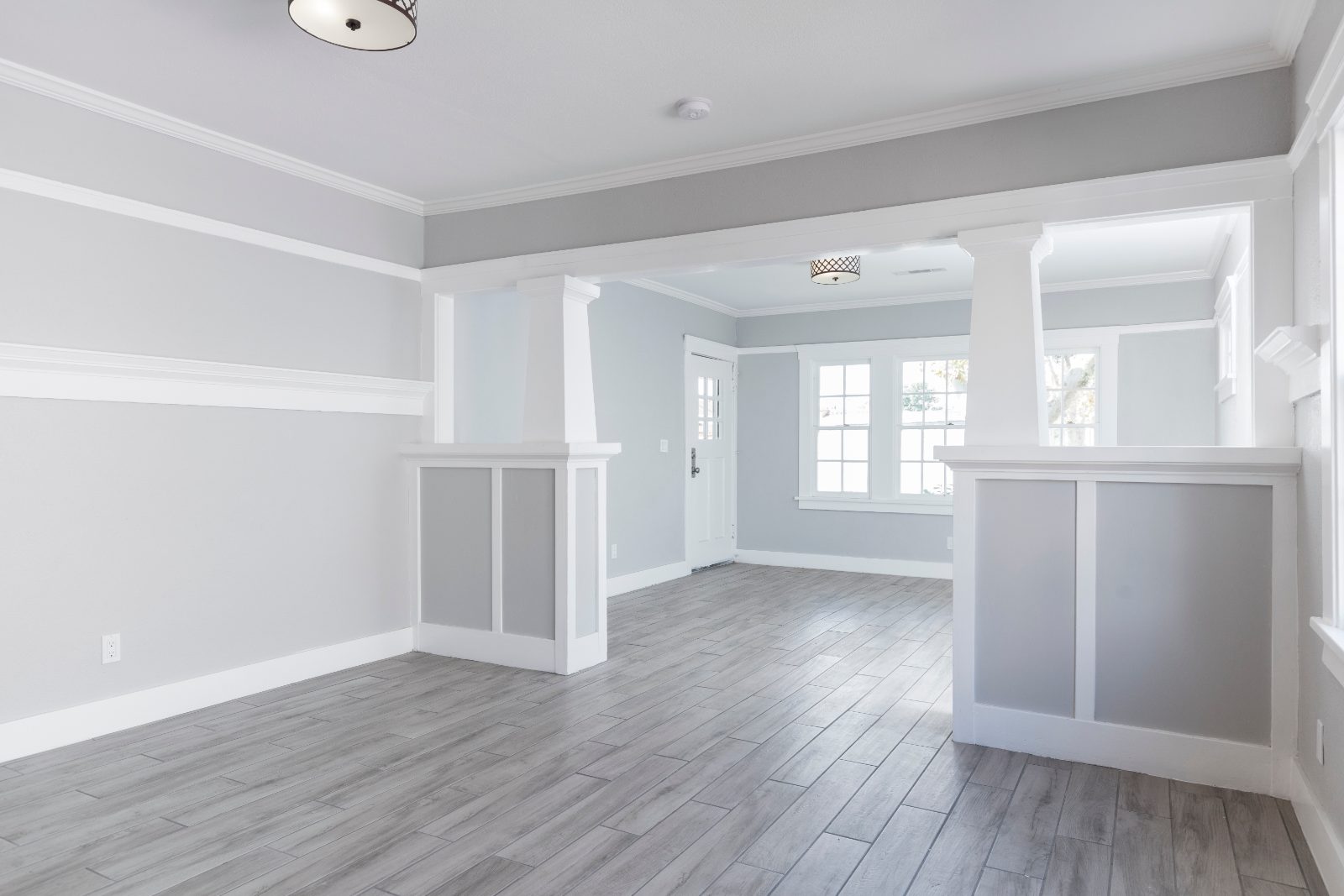 Empty open-concept room with gray and white wainscoting, wood flooring, and large windows