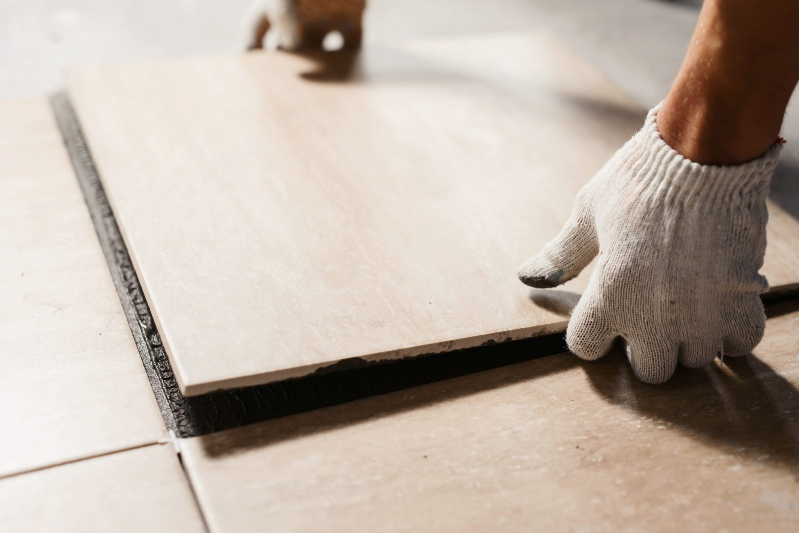 Worker in white gloves installing large ceramic floor tile with black trim edge