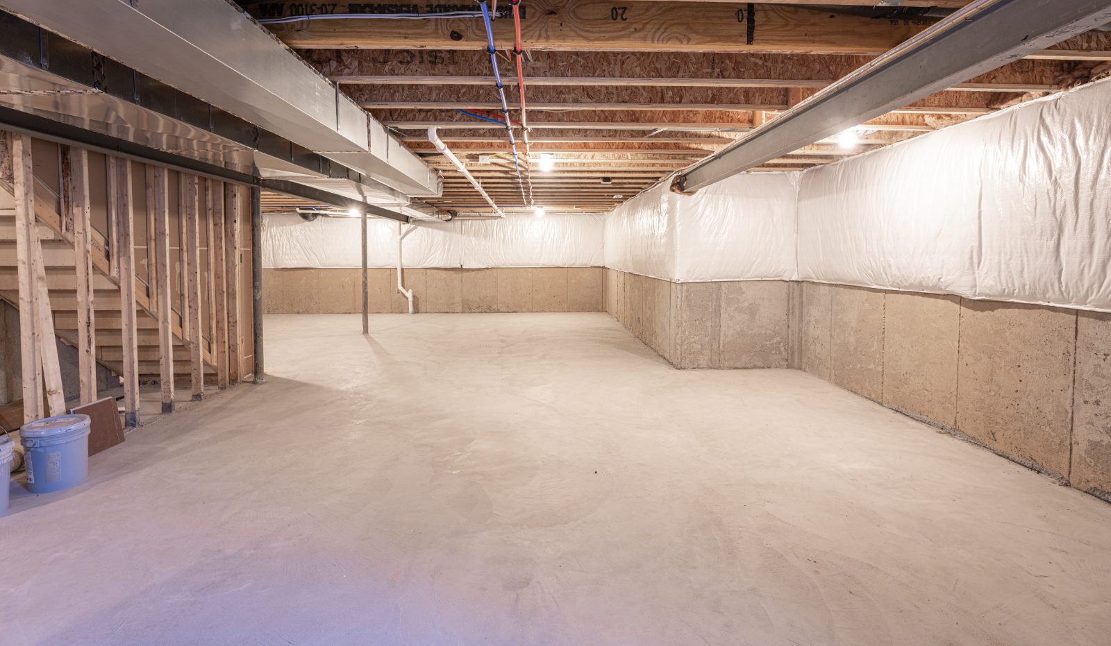 Unfinished basement space with concrete floor, exposed wooden beams, white plastic sheeting, and metal support columns