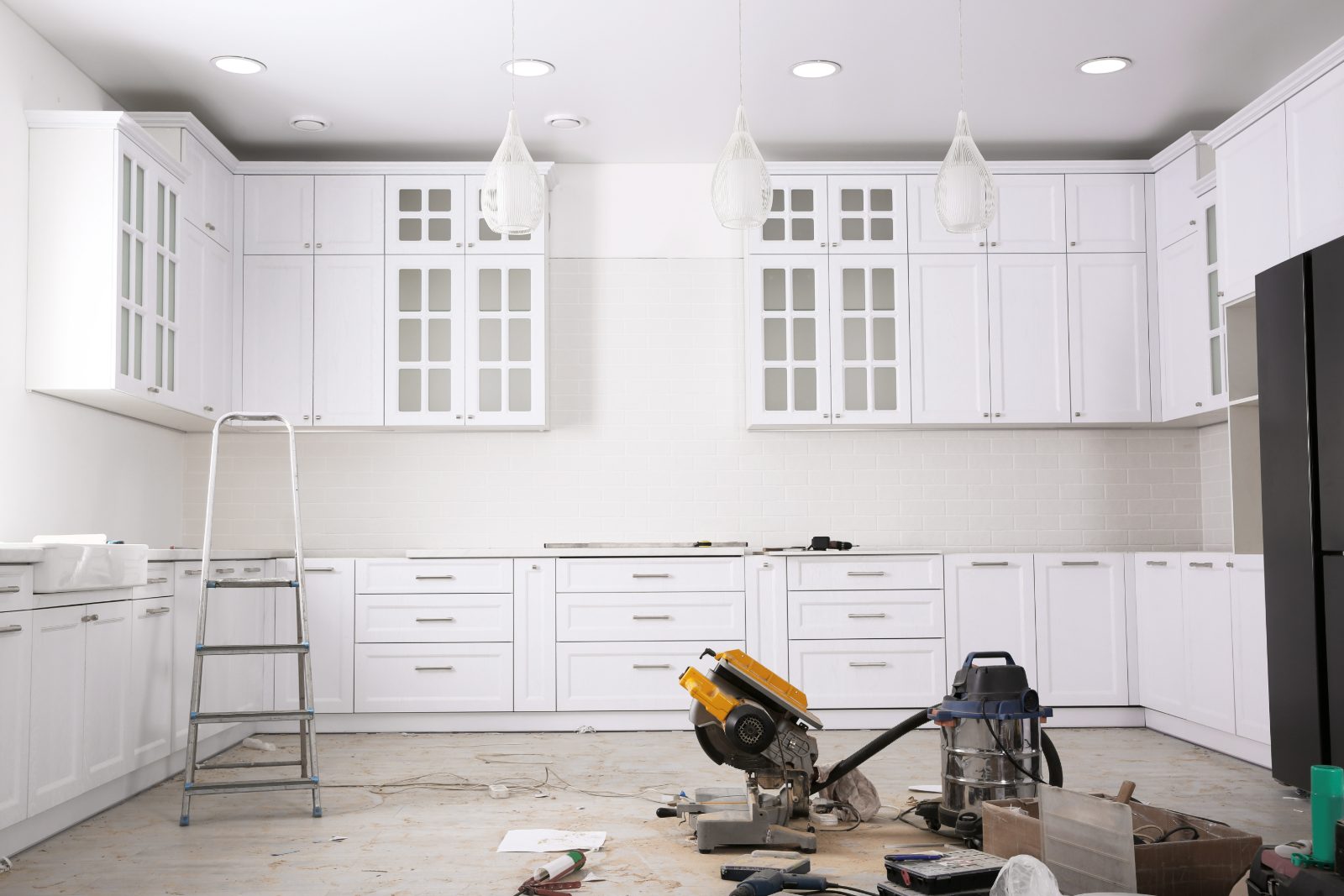 Kitchen renovation in progress with white cabinetry, construction tools, and ladder on wooden floor